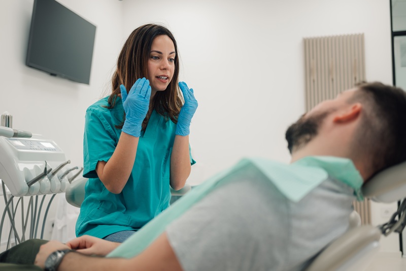 Female dentist wearing gloves explaining dental procedure to male patient lying on dental chair in dental emergency