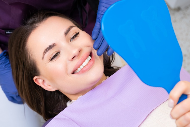 Smiling woman patient looks in the mirror after bonding.