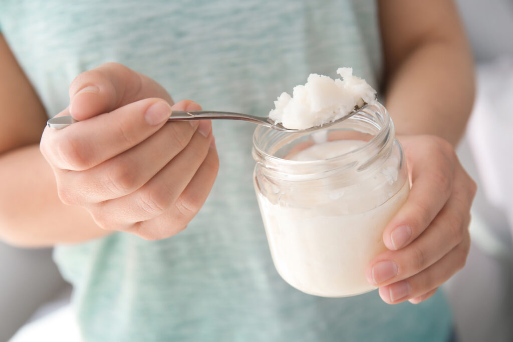Woman scooping a spoonful of coconut oil from a glass jar for oil pulling