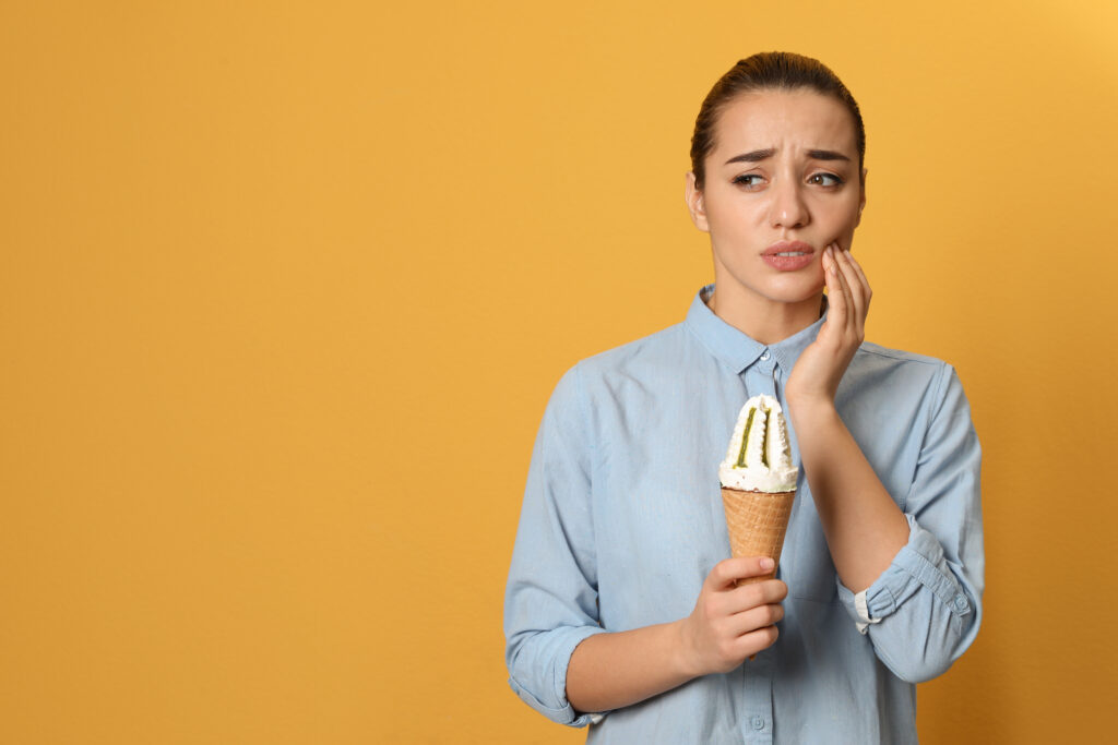 Young woman holding her cheek in pain from cracked tooth syndrome after biting into an ice cream cone