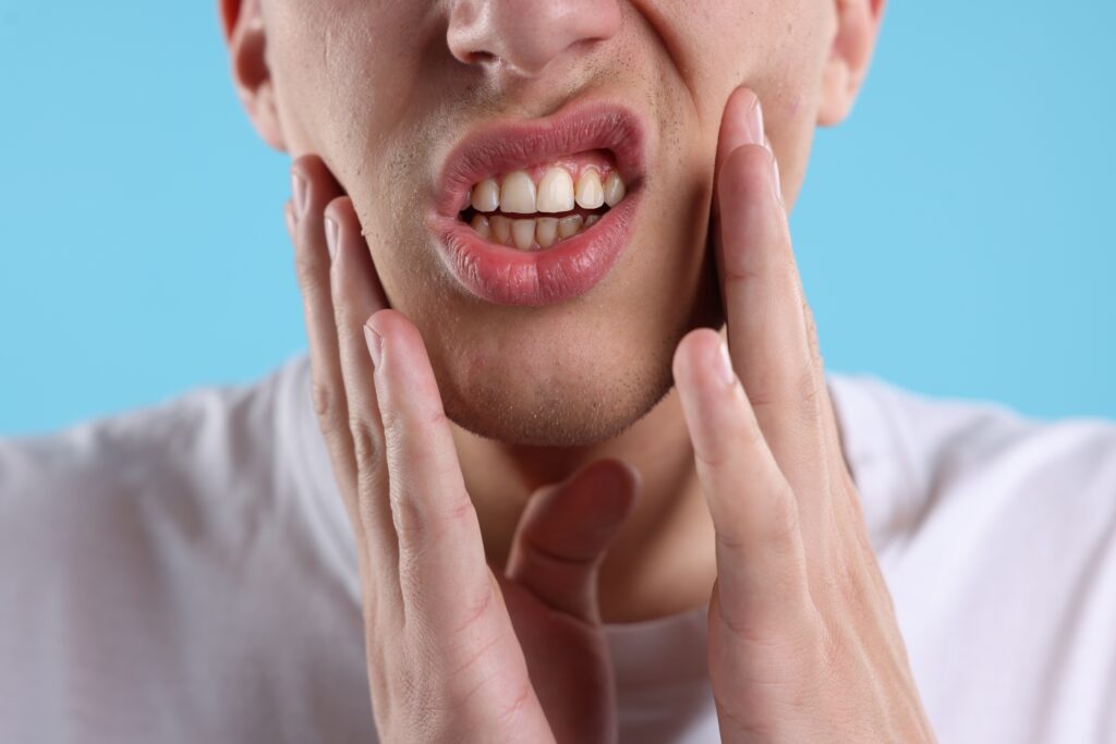 Man holding both sides of his jaw in discomfort, a common sign of tooth sensitivity linked to tooth erosion